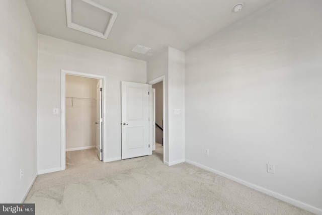 unfurnished bedroom featuring a walk in closet, a closet, and light colored carpet