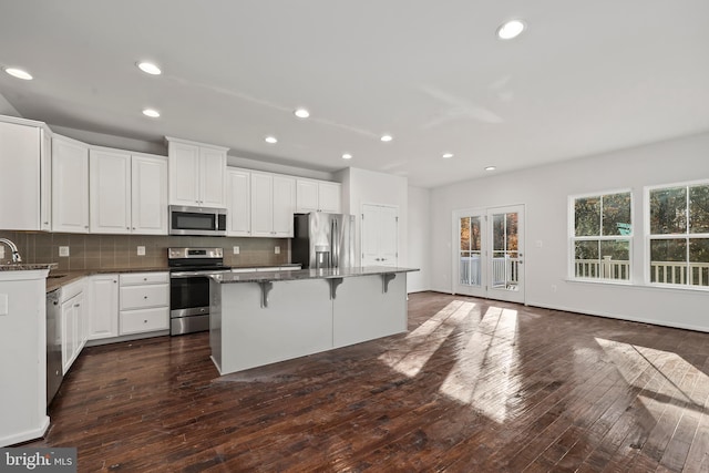 kitchen with a center island, stainless steel appliances, a kitchen bar, decorative backsplash, and white cabinetry