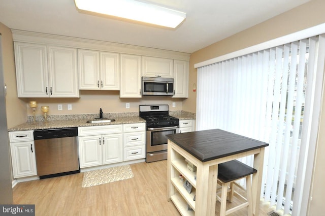 kitchen with light stone countertops, light hardwood / wood-style floors, white cabinets, appliances with stainless steel finishes, and sink