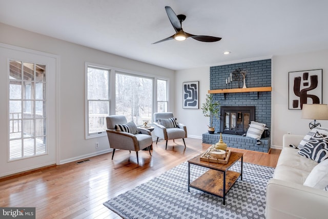 living room with a fireplace, wood finished floors, visible vents, and baseboards