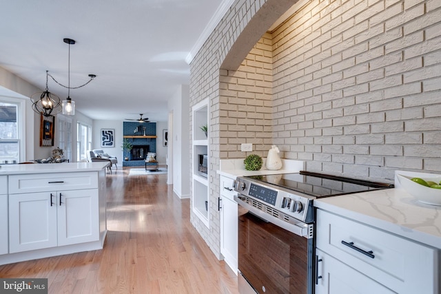 kitchen with a brick fireplace, white cabinets, electric stove, and decorative light fixtures