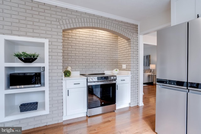 kitchen featuring stainless steel appliances, white cabinetry, light wood-style floors, light countertops, and ornamental molding