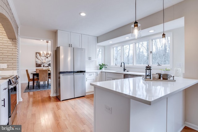 kitchen with a peninsula, appliances with stainless steel finishes, white cabinets, and light countertops