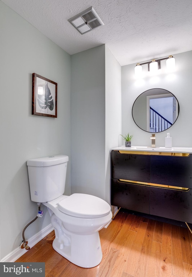 bathroom with a textured ceiling, toilet, wood finished floors, vanity, and visible vents