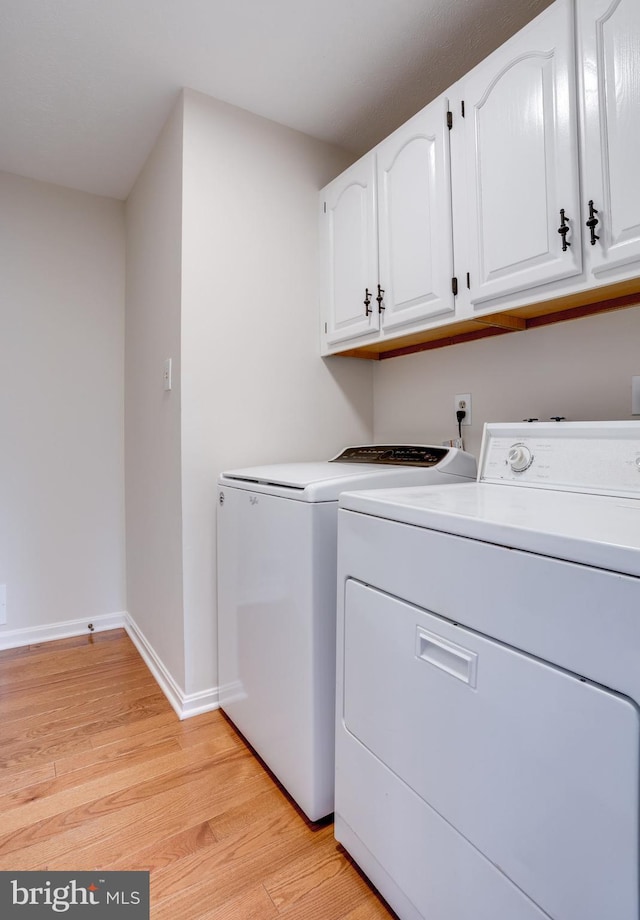 laundry area featuring baseboards, washing machine and clothes dryer, cabinet space, and light wood-style floors