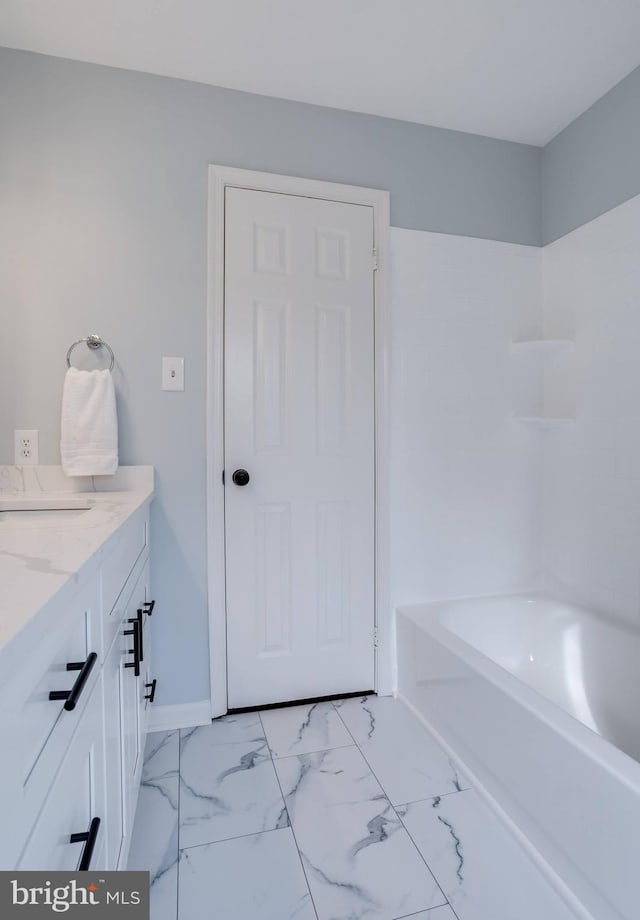 bathroom featuring marble finish floor, vanity, baseboards, and a bathing tub