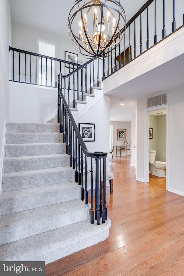 stairway featuring wood finished floors, a towering ceiling, visible vents, baseboards, and an inviting chandelier