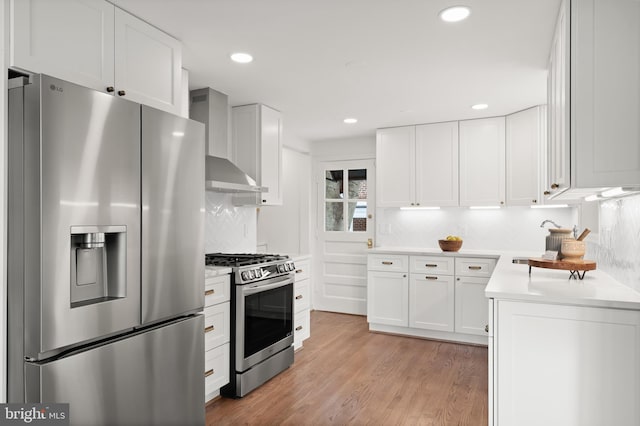 kitchen featuring stainless steel appliances, white cabinets, wall chimney exhaust hood, tasteful backsplash, and light hardwood / wood-style floors