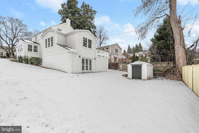 snow covered rear of property featuring french doors and a storage unit