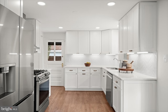 kitchen featuring stainless steel appliances, light hardwood / wood-style floors, tasteful backsplash, white cabinets, and sink