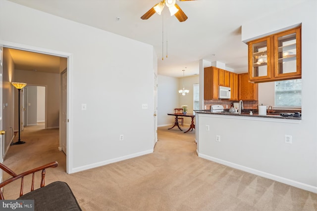 kitchen with white microwave, light carpet, ceiling fan with notable chandelier, backsplash, and brown cabinets