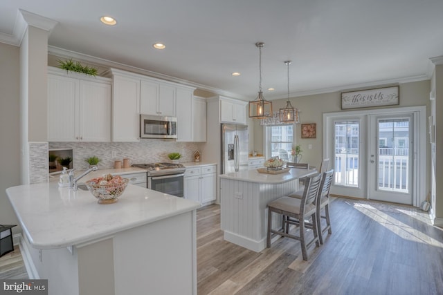 kitchen with a kitchen breakfast bar, stainless steel appliances, pendant lighting, a kitchen island, and white cabinets