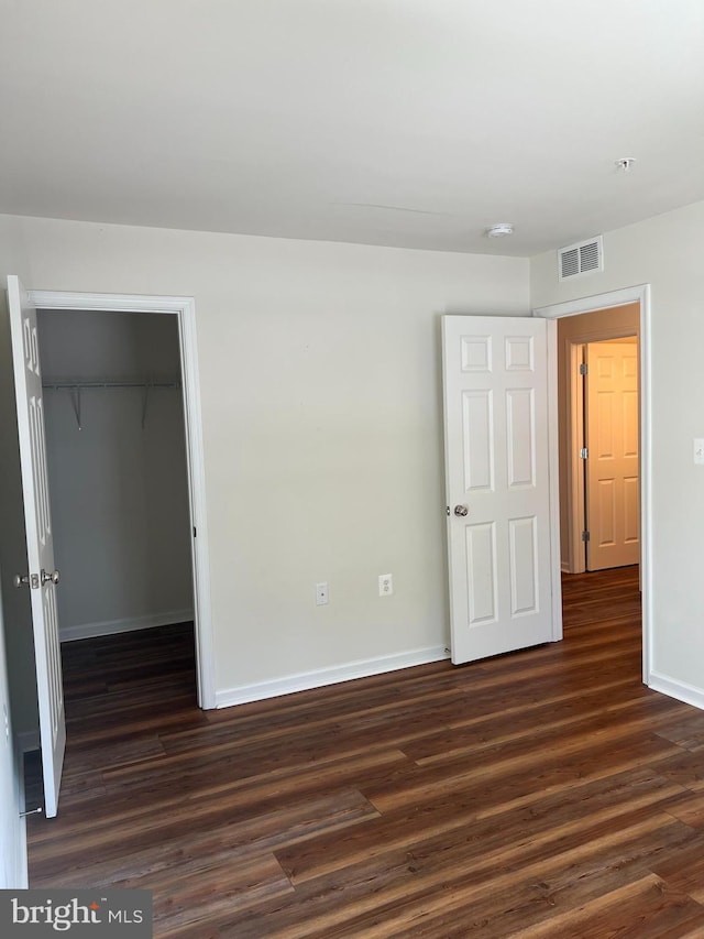 unfurnished bedroom with dark hardwood / wood-style flooring, a spacious closet, and a closet