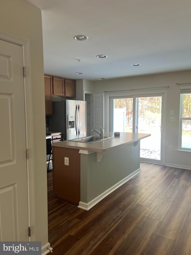 kitchen with stainless steel fridge, a kitchen island with sink, and dark hardwood / wood-style floors