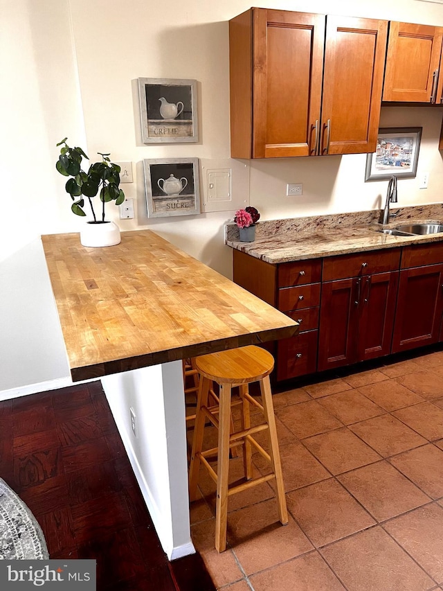 kitchen with tile patterned flooring, light stone countertops, sink, and a kitchen bar