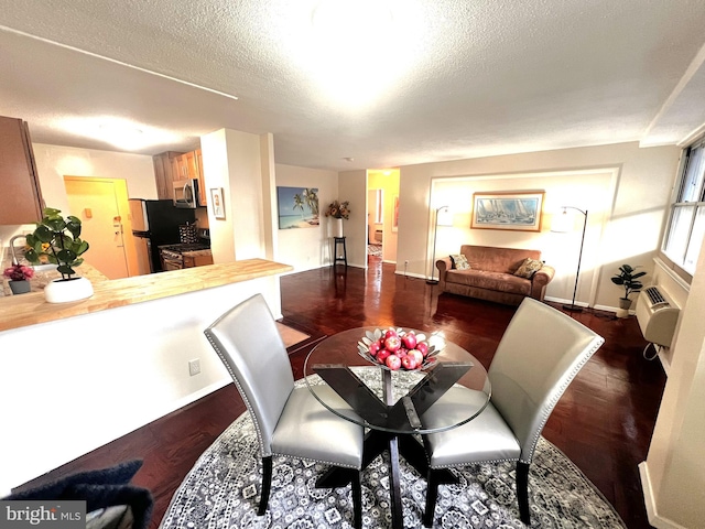 dining room featuring dark wood-type flooring, a textured ceiling, and an AC wall unit