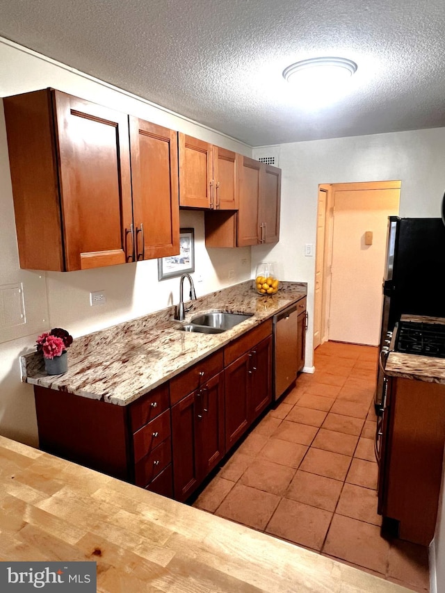 kitchen featuring sink, dishwasher, light stone countertops, gas range oven, and black fridge