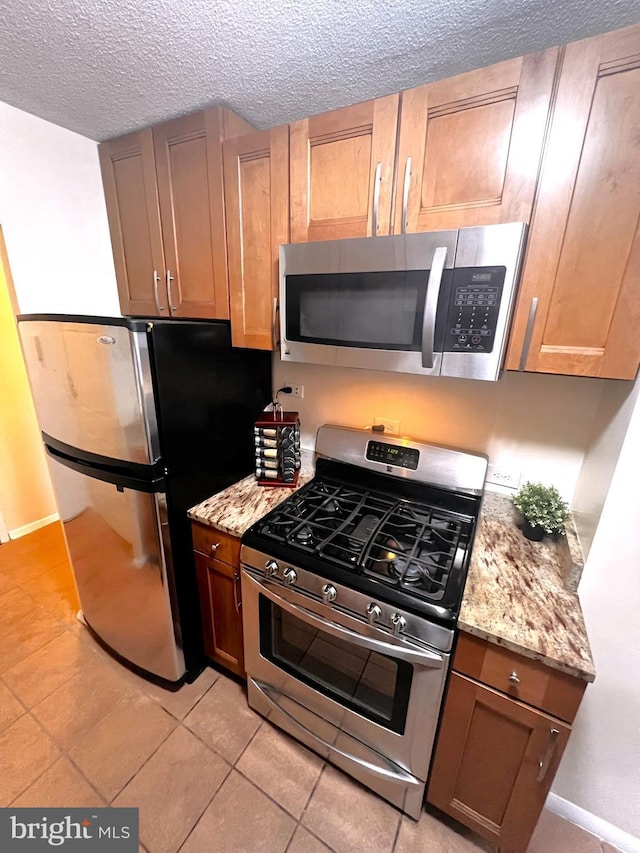 kitchen featuring light stone counters, appliances with stainless steel finishes, light tile patterned flooring, and a textured ceiling