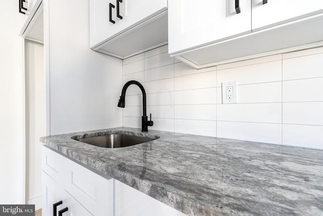 kitchen featuring white cabinets, dark stone counters, backsplash, and sink