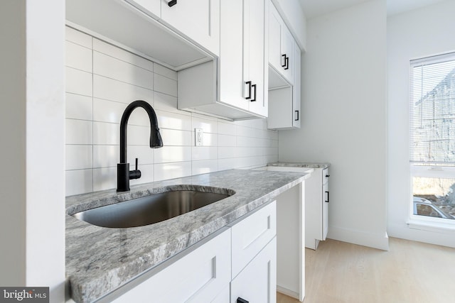 kitchen with white cabinets, light stone counters, decorative backsplash, sink, and light hardwood / wood-style flooring