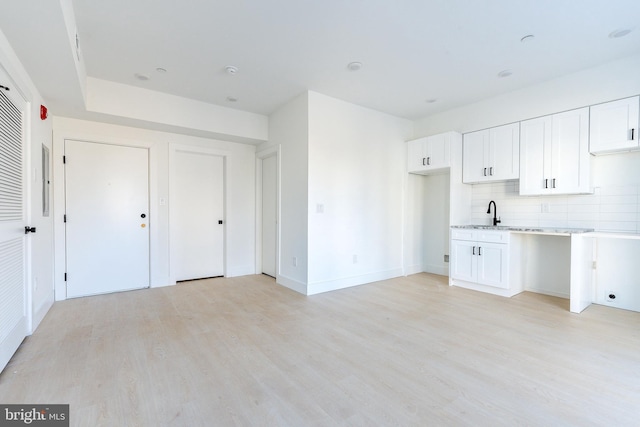 kitchen featuring white cabinets, decorative backsplash, light wood-type flooring, and light stone counters