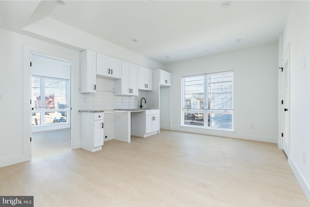 kitchen featuring plenty of natural light, white cabinets, light wood-type flooring, and decorative backsplash