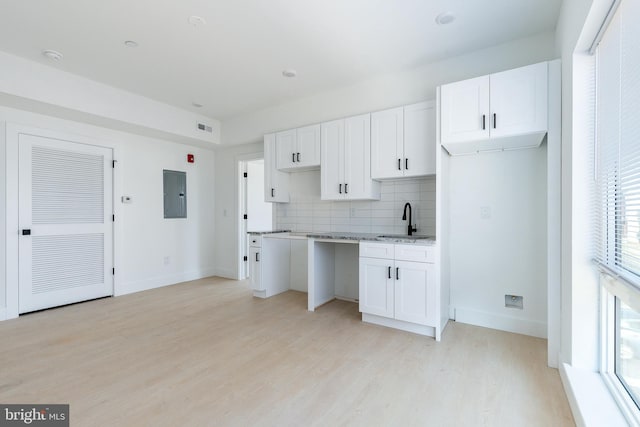 kitchen featuring sink, white cabinetry, electric panel, light hardwood / wood-style flooring, and backsplash