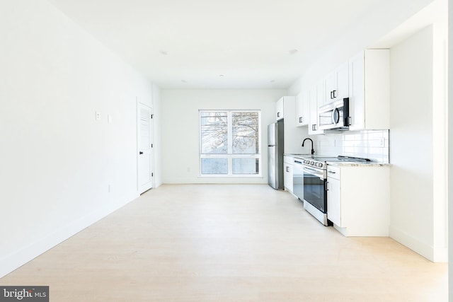 kitchen featuring appliances with stainless steel finishes, white cabinets, light hardwood / wood-style flooring, backsplash, and sink