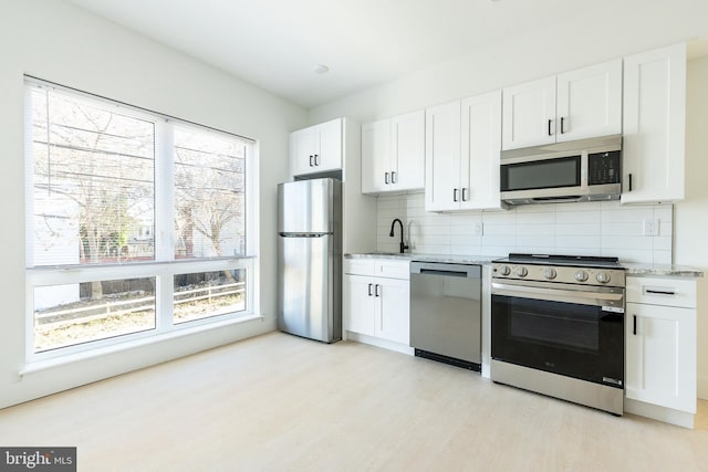 kitchen featuring light stone counters, stainless steel appliances, white cabinetry, and backsplash