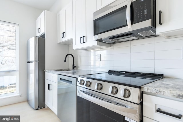 kitchen with sink, appliances with stainless steel finishes, light stone counters, and white cabinetry