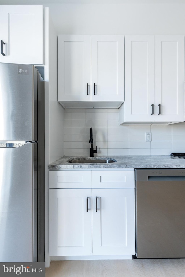 kitchen featuring stainless steel appliances, sink, white cabinetry, tasteful backsplash, and light stone countertops