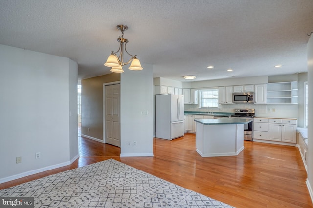 kitchen featuring white cabinetry, light wood-type flooring, tasteful backsplash, hanging light fixtures, and appliances with stainless steel finishes