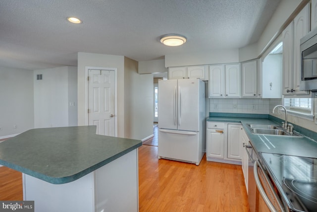 kitchen featuring stainless steel appliances, tasteful backsplash, light wood-type flooring, white cabinetry, and sink