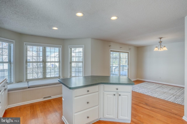 kitchen with a textured ceiling, pendant lighting, light hardwood / wood-style floors, an inviting chandelier, and white cabinets