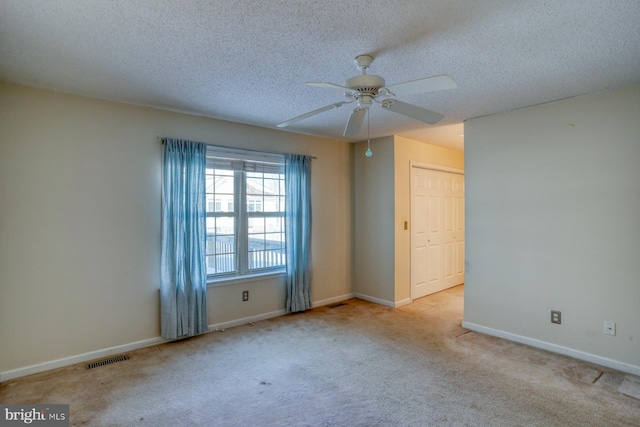 empty room with a textured ceiling, light colored carpet, and ceiling fan