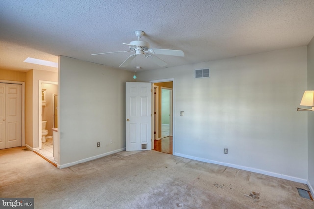 carpeted empty room featuring a textured ceiling, ceiling fan, and a skylight