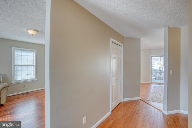 corridor featuring a textured ceiling, light hardwood / wood-style flooring, and a wealth of natural light