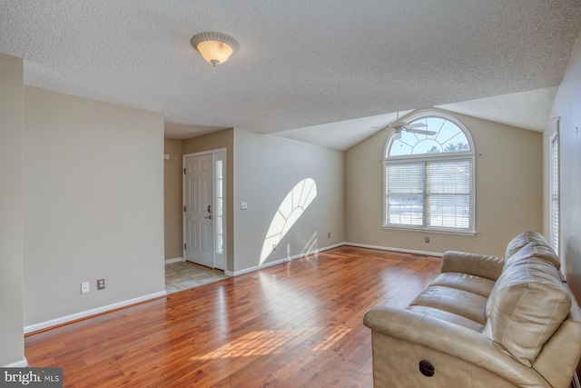 living room with a textured ceiling, ceiling fan, light hardwood / wood-style flooring, and lofted ceiling