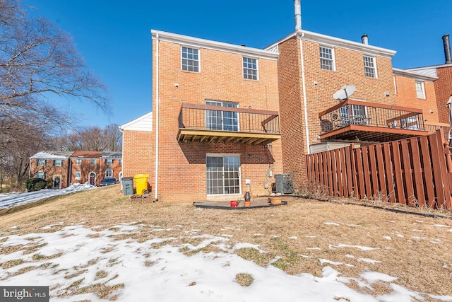 snow covered back of property with a balcony and central AC unit