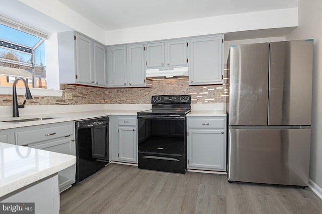 kitchen with gray cabinets, black appliances, light wood-type flooring, decorative backsplash, and sink