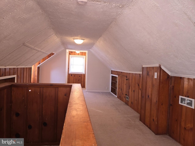 additional living space with a textured ceiling, vaulted ceiling, light colored carpet, and wood walls