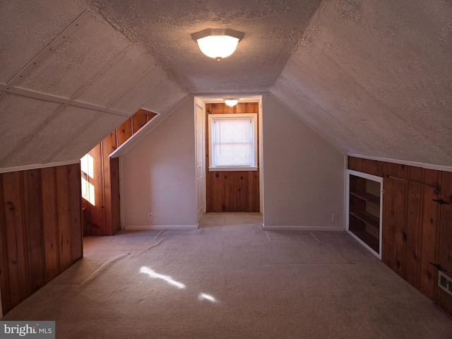 bonus room with a textured ceiling, vaulted ceiling, light carpet, and wooden walls