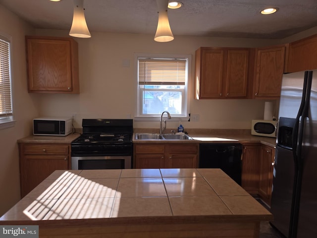 kitchen with a center island, sink, hanging light fixtures, stainless steel appliances, and tile counters