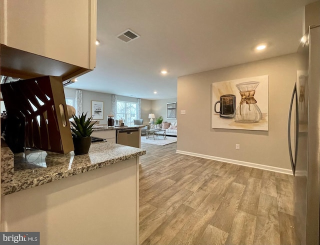 kitchen with kitchen peninsula, light stone countertops, light hardwood / wood-style flooring, stainless steel appliances, and white cabinetry