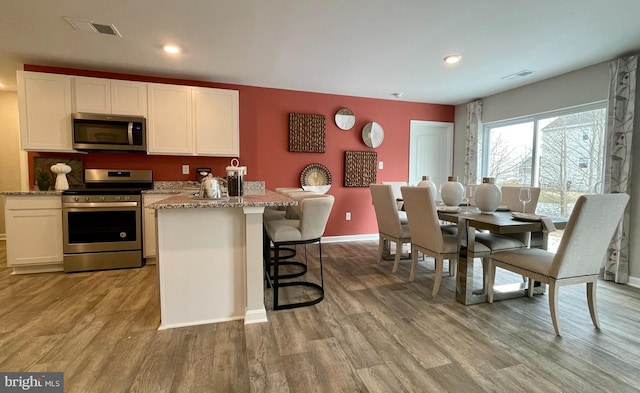 kitchen featuring white cabinets, light wood-type flooring, appliances with stainless steel finishes, and light stone countertops