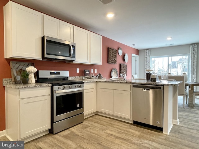 kitchen featuring white cabinetry, light stone counters, light hardwood / wood-style floors, kitchen peninsula, and appliances with stainless steel finishes