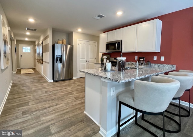 kitchen with stainless steel appliances, white cabinets, light stone counters, a kitchen bar, and light hardwood / wood-style floors