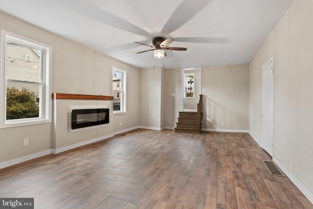 unfurnished living room with dark wood-type flooring, ceiling fan, and a wealth of natural light