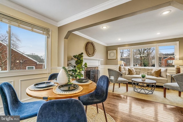 dining space with a brick fireplace, a wealth of natural light, ornamental molding, and hardwood / wood-style floors