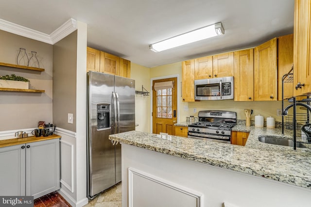 kitchen with sink, crown molding, appliances with stainless steel finishes, light stone countertops, and kitchen peninsula